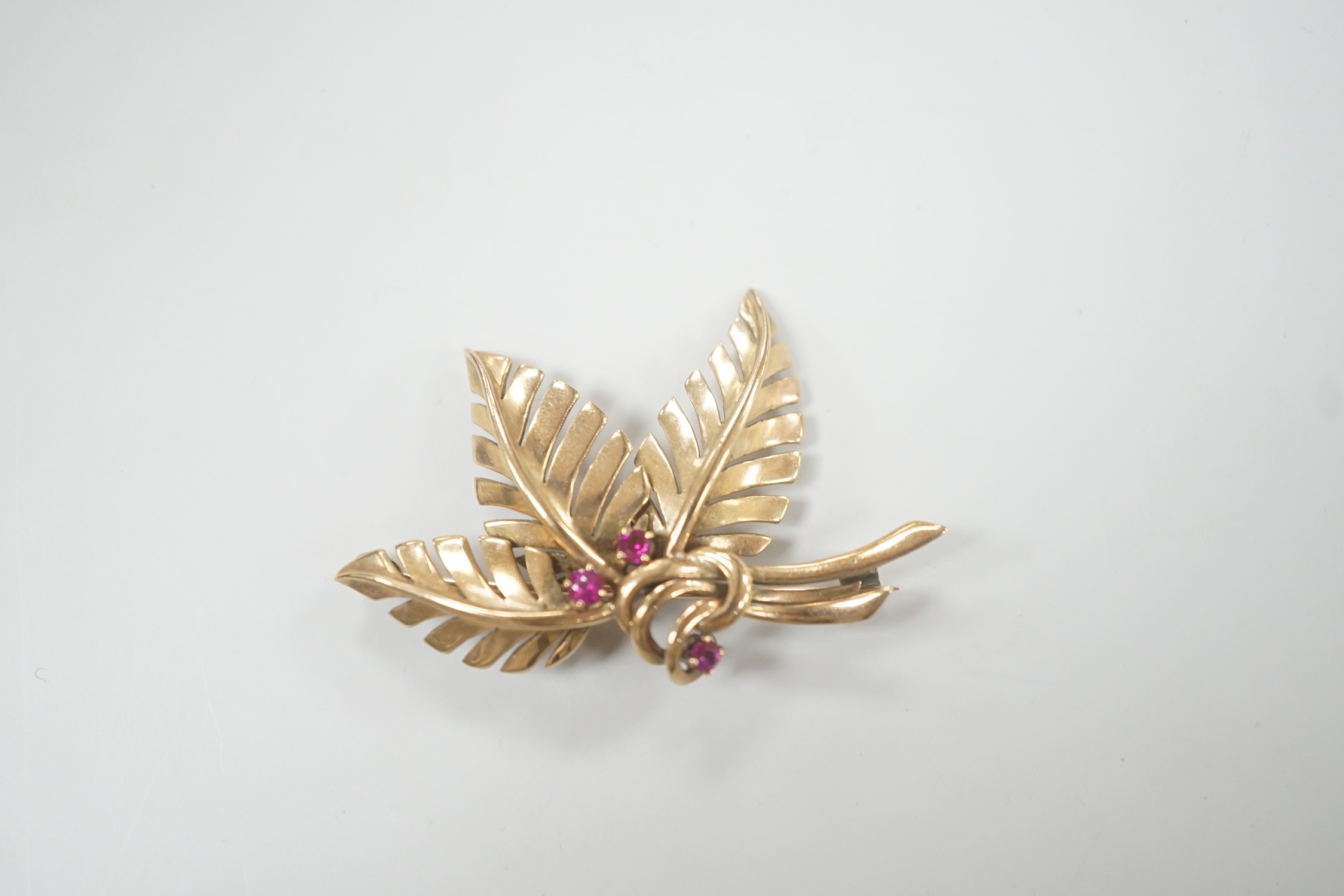 A yellow metal and three stone ruby set foliate brooch, 45mm, gross weight 6.8 grams.